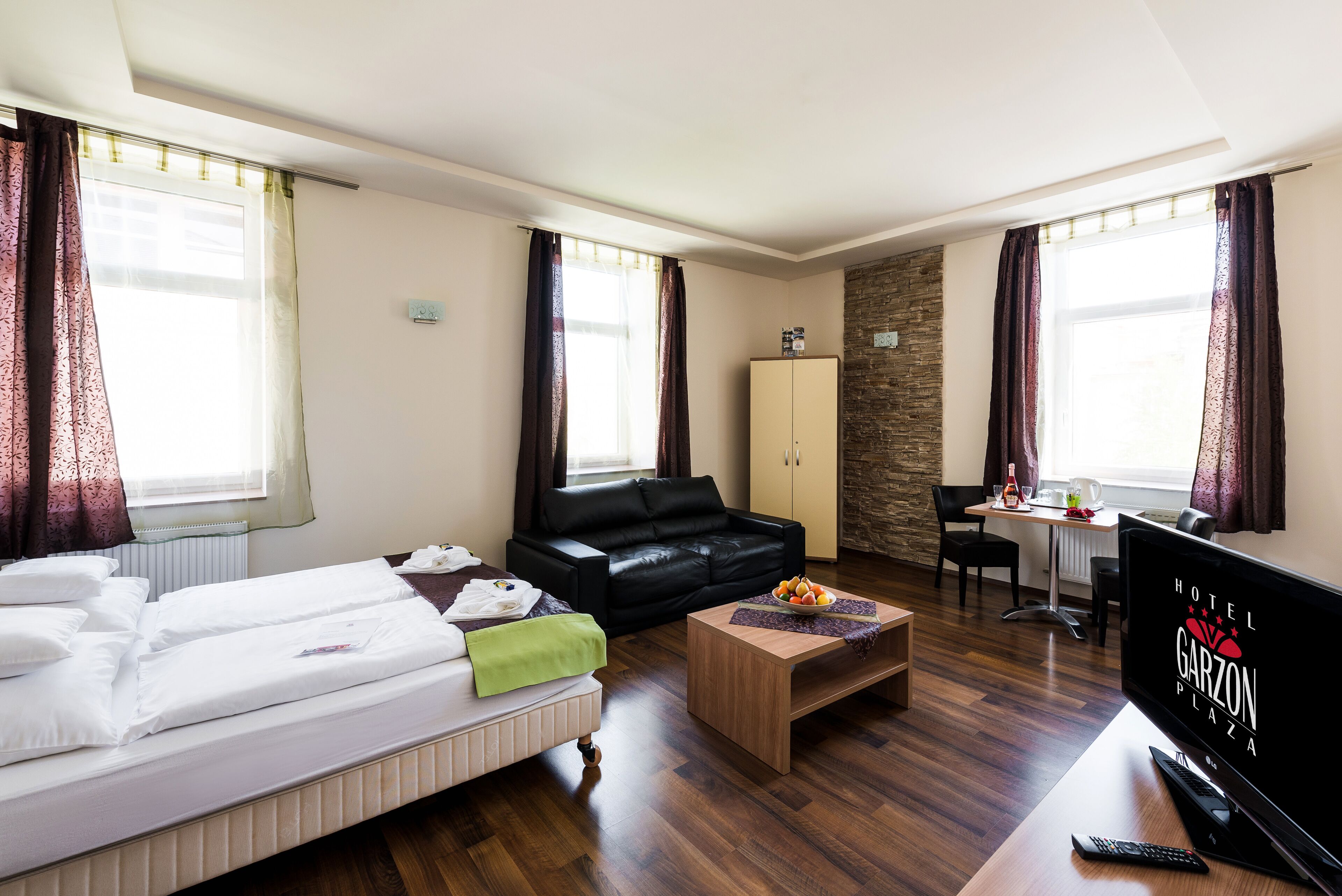 A hotel room with a bed, a sofa, a desk, a TV, and a stone wall.