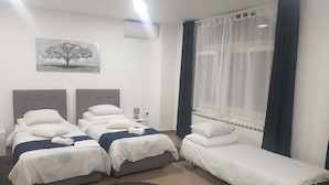 Ein Hotelzimmer mit zwei Betten, einem großen Fenster mit Vorhängen, einem Heizkörper und einem Bild an der Wand.