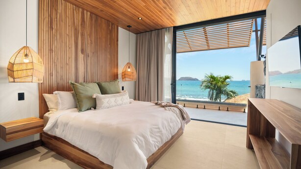 Quarto com cama grande, paredes de painel de madeira, vista para o oceano e teto de madeira.
