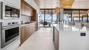 Cozinha moderna com eletrodomésticos de aço inoxidável, armários de madeira e vista para o oceano.