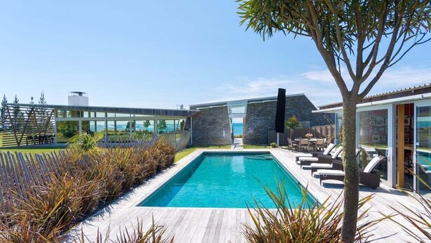 Un área de piscina moderna con vista despejada, sillas de descanso y una estructura de vidrio.