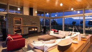 Una sala de estar moderna con una chimenea de piedra, asientos cómodos y grandes ventanales con vistas al exterior.