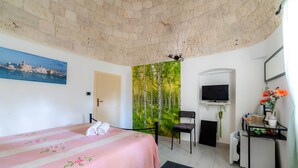 A bedroom with a bed, a chair, a TV, and a small table with a vase of flowers. - La Maison-D B&B (Monopoli)