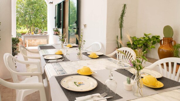A dining area with white chairs, a long table set with yellow and white plates, glasses, and cutlery. - La Maison-D B&B (Monopoli)