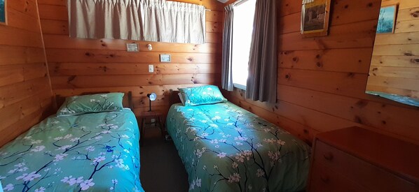 A cabin room with two beds, wooden walls, and a window with curtains.