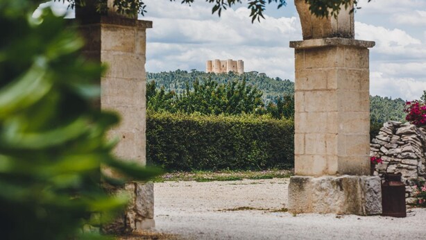 A stone archway leading to a castle on a hill, surrounded by greenery and a clear sky. - Ai Pilieri di Bagnoli (Andria)