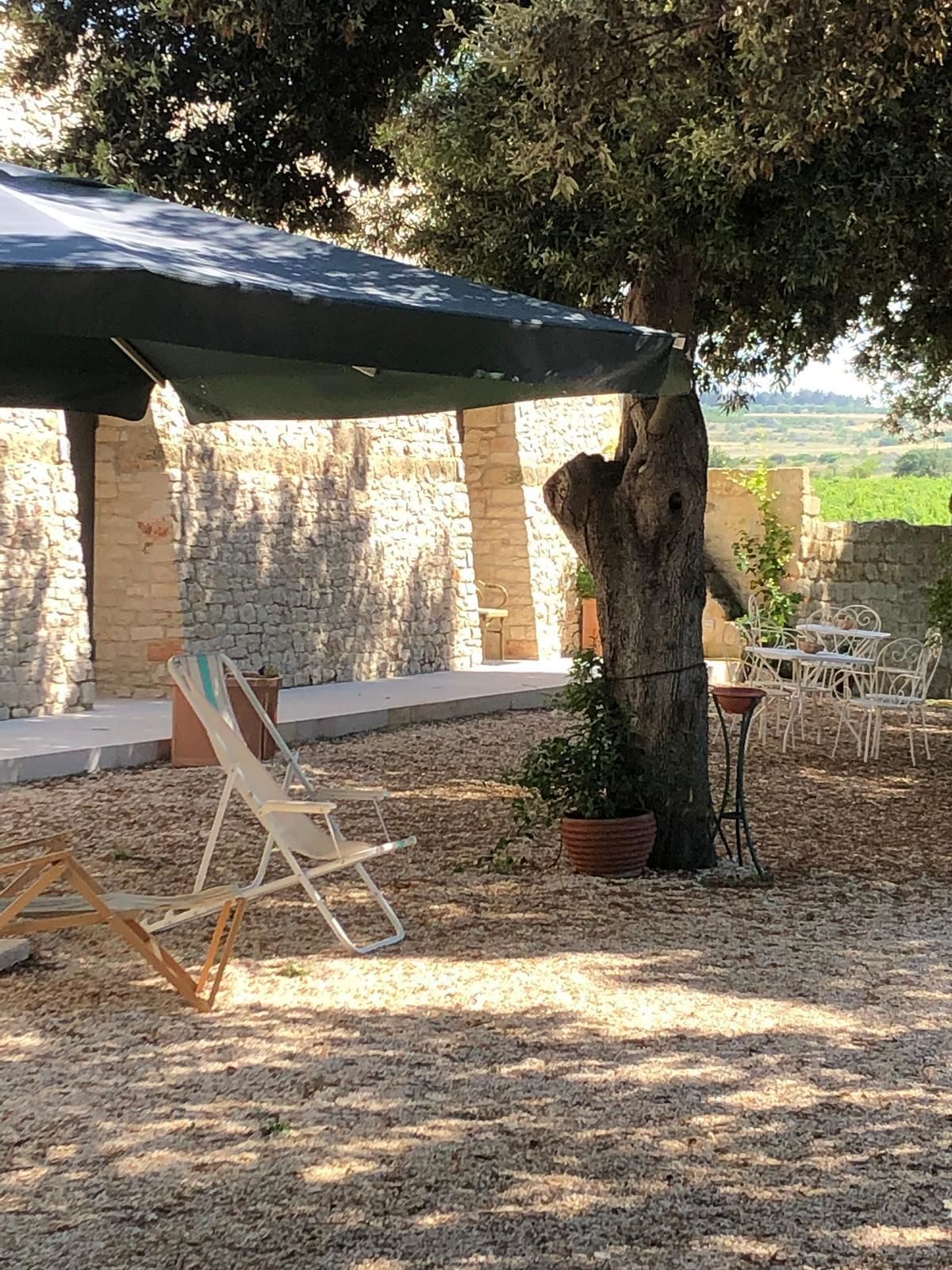 A covered outdoor seating area with stone walls, a tree, and a view of the countryside.