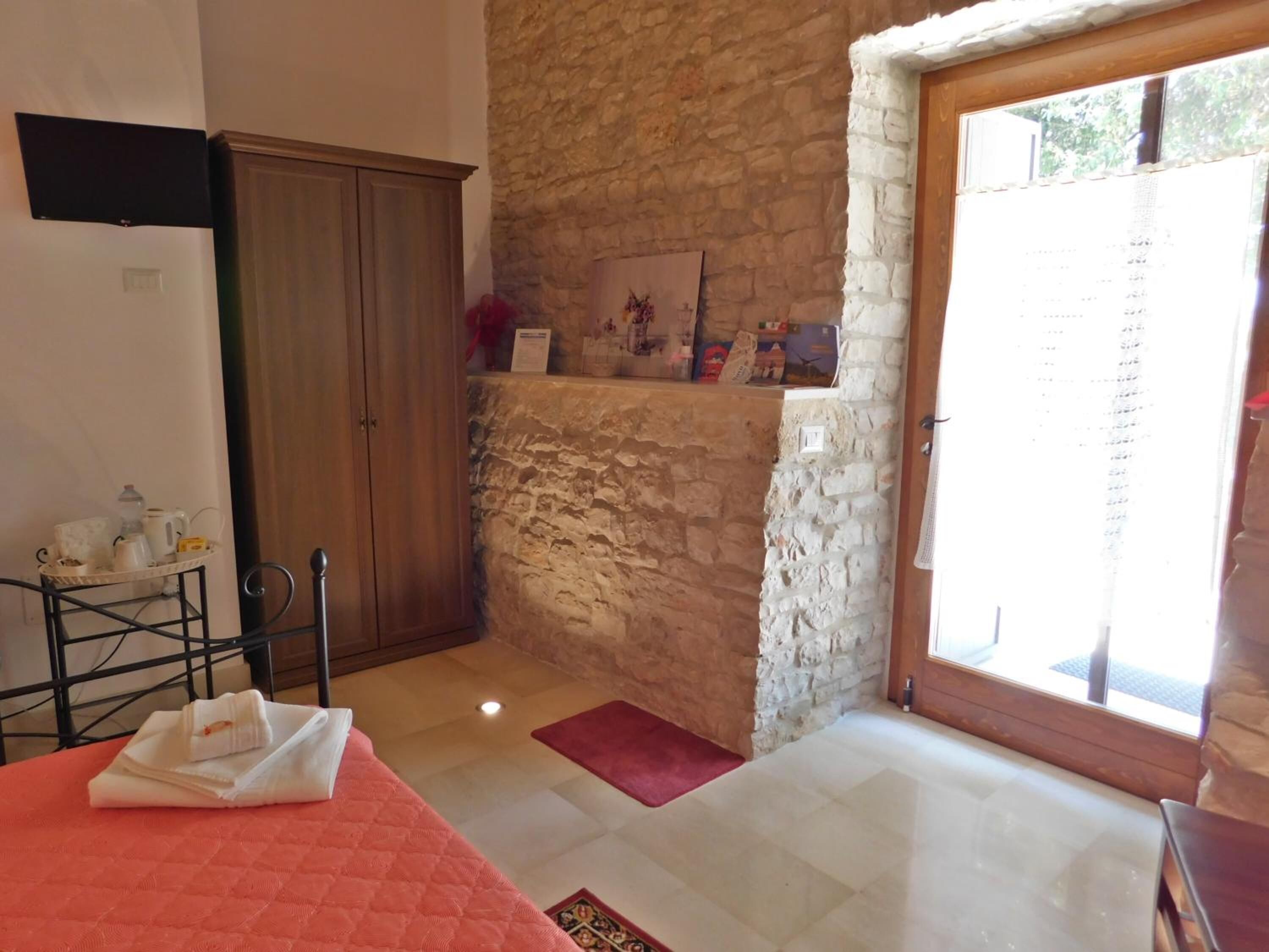 A room with a bed, a wooden wardrobe, a stone wall, and a door leading to a balcony.