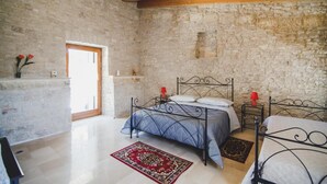 A bedroom with stone walls, a wooden ceiling, a bed with a metal frame, a bedside table with a red lamp, and a red and black rug. - Ai Pilieri di Bagnoli (Andria)