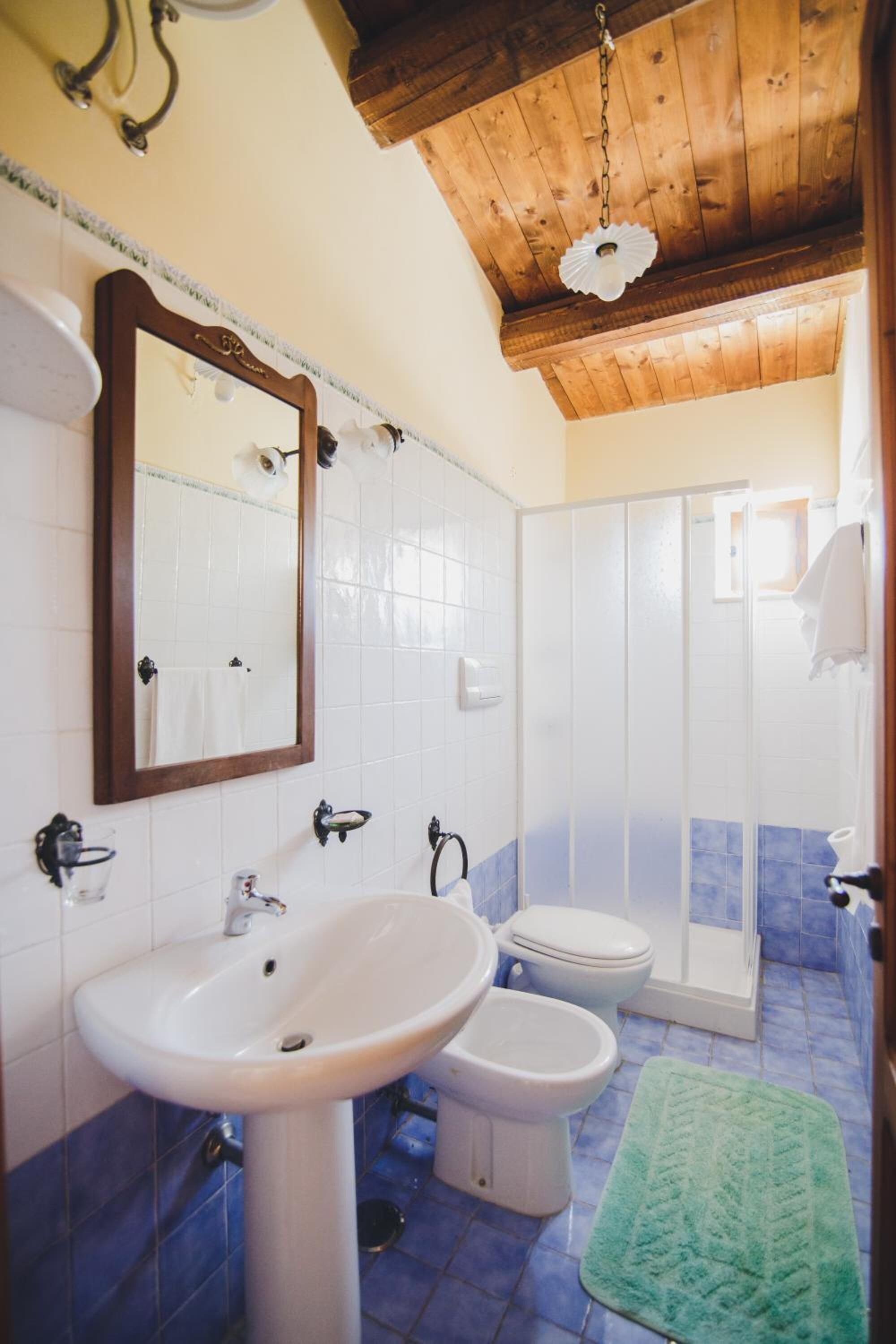 A bathroom with a wooden ceiling, a sink, a mirror, a toilet, and a shower.