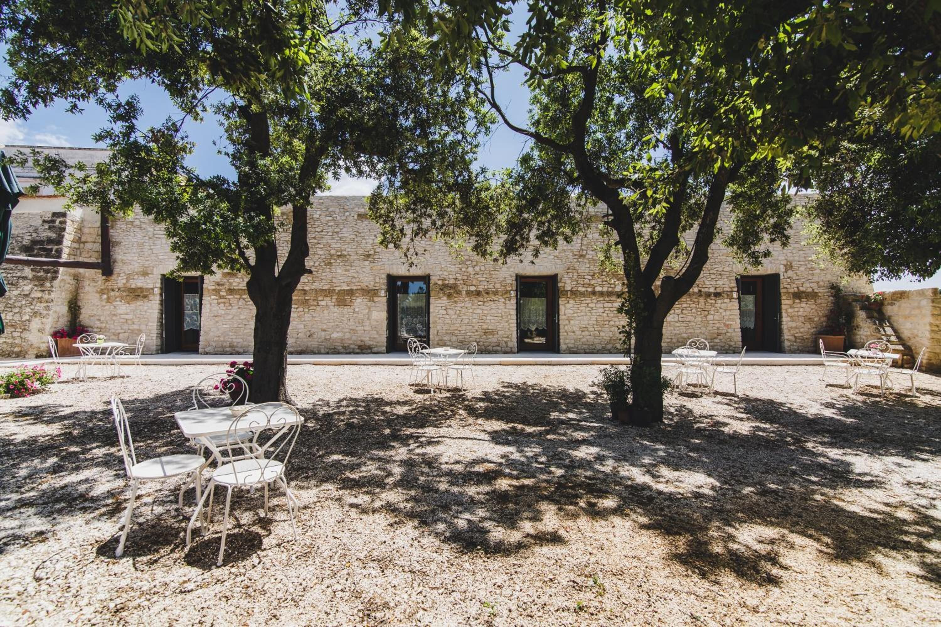 An outdoor patio with stone walls, trees, and white metal chairs.