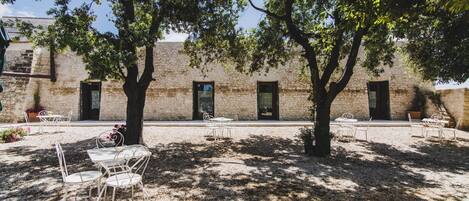 An outdoor patio with stone walls, trees, and white metal chairs.