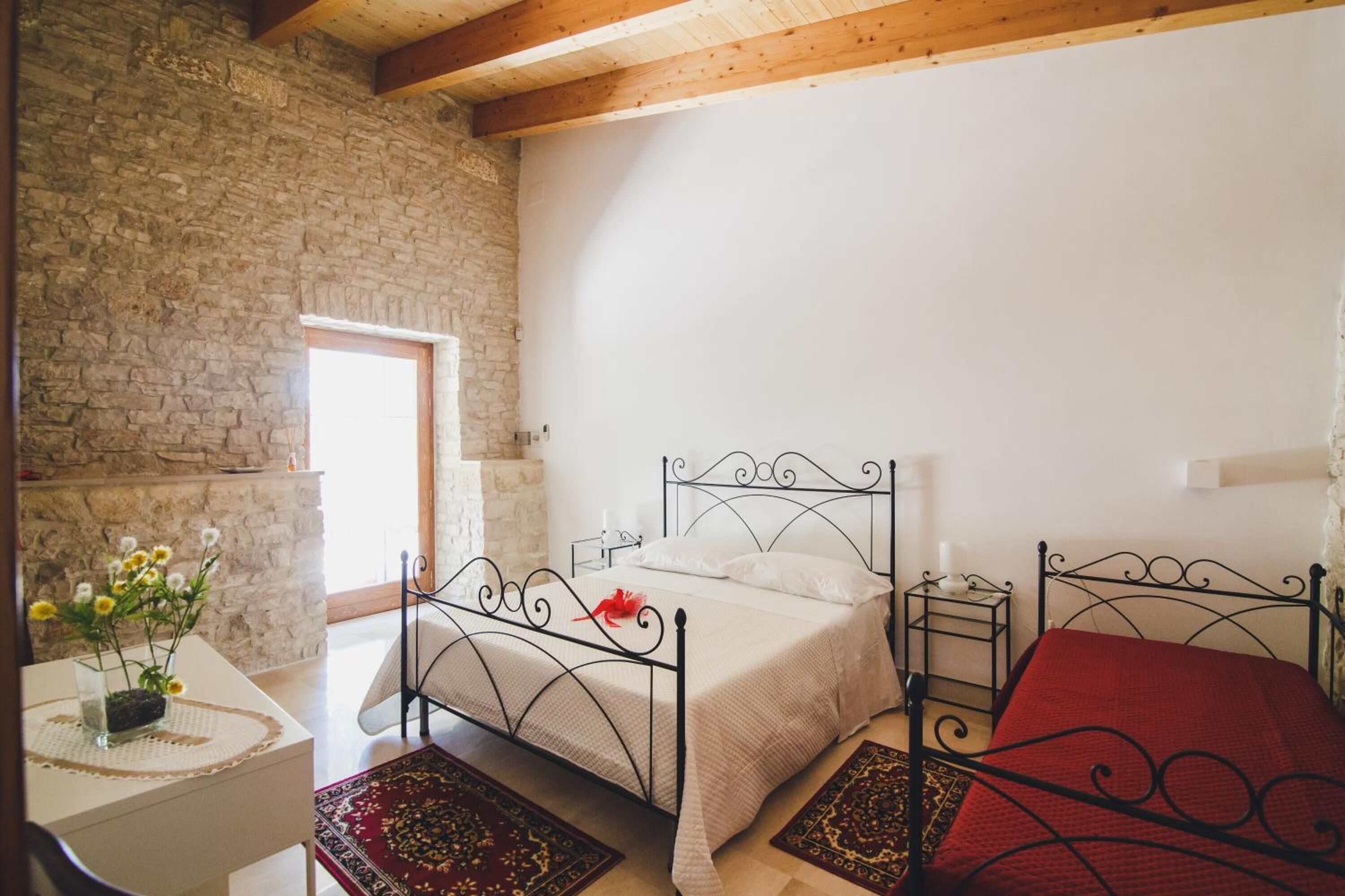 A bedroom with a stone wall, a bed with a metal frame, a bedside table, and a red rug.