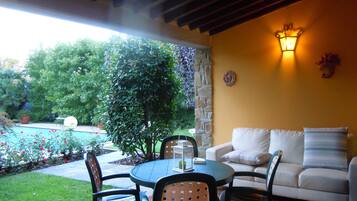 Una terrazza esterna con un tavolo rotondo, sedie e un divano. Si nota un pilastro in pietra, un punto luce a parete e una pianta in vaso.