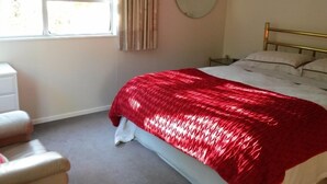 A bedroom with a bed, a bedside table, a chair, a window with curtains, and a round mirror on the wall. - Peaceful, sunny, furnished - everything you need. (Johnsonville)
