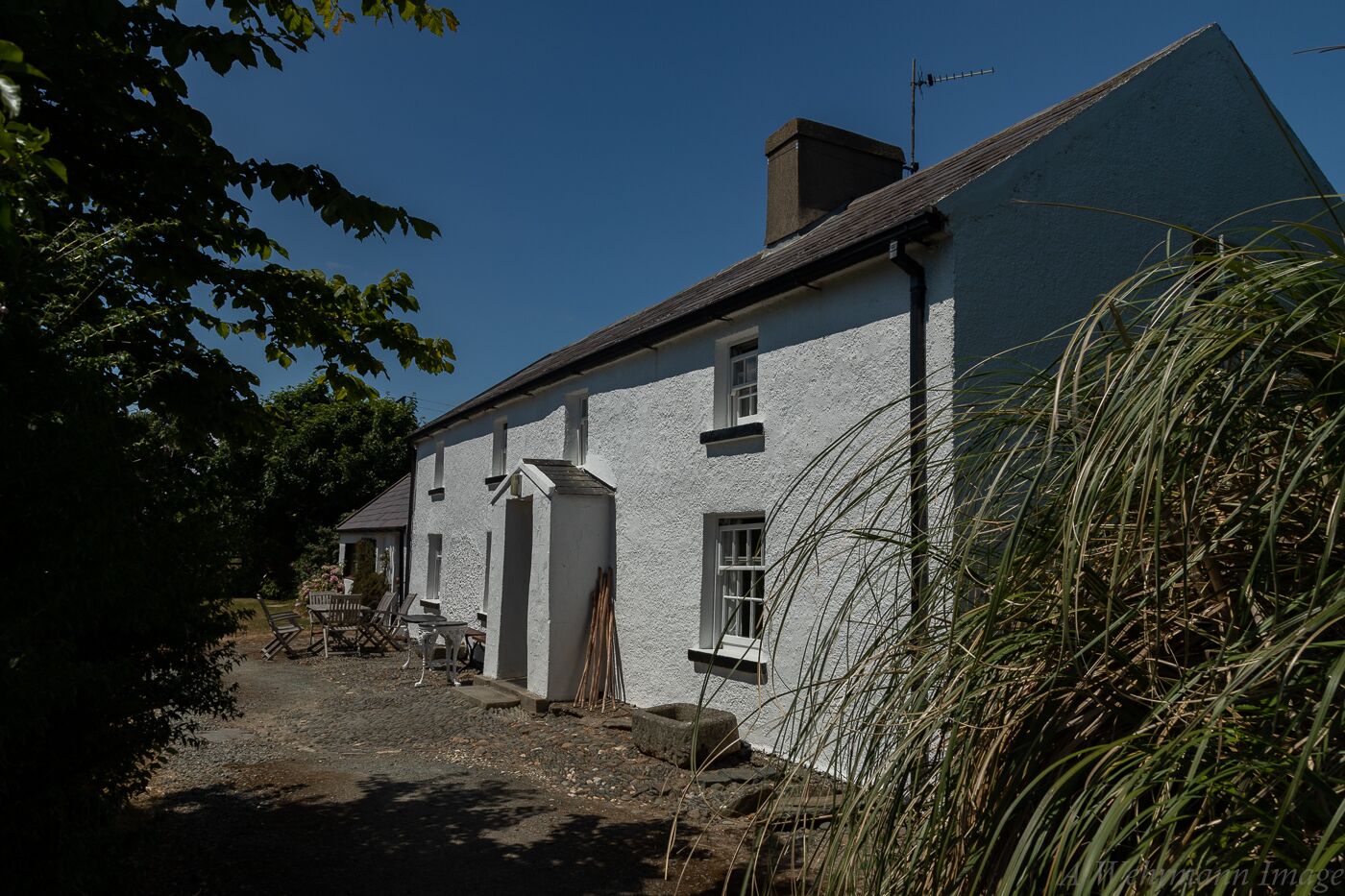 A traditional white building with a sloped roof, a chimney, and a small porch area with chairs.