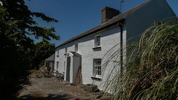 A traditional white building with a sloped roof, a chimney, and a small porch area with chairs.