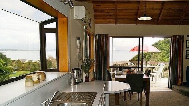 A kitchen with a view of the sea, a dining area with a table and chairs, and a large sliding glass door leading to an outdoor patio.
