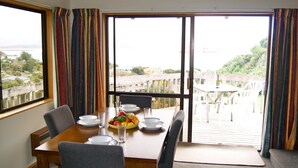 A dining area with a table set for four, a view of a deck and greenery outside, and a window with curtains.