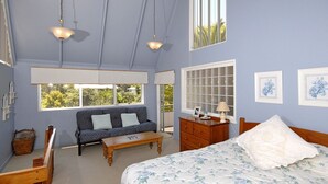 Une chambre à coucher comprenant un lit, un canapé, une commode en bois, un bureau et deux fenêtres.
