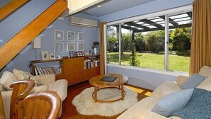 Un salon moderne doté d’un haut plafond, d’une bibliothèque intégrée, d’une table basse ronde et d’une grande fenêtre donnant sur un jardin.