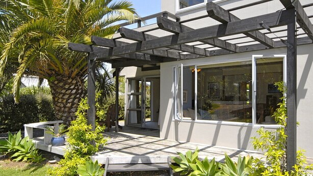 Une maison moderne dotée d’un patio couvert, de grandes fenêtres et d’une végétation luxuriante.