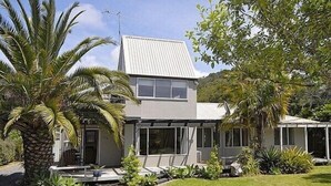 Une maison moderne à deux étages, dotée d’une grande façade vitrée, entourée d’une végétation luxuriante et d’une pelouse bien entretenue.