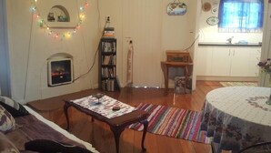A cozy living room with a fireplace, a bookshelf, and a dining area with a table. - Historic summer house by the sea (Castlecliff)