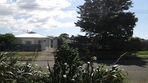 A gated residential area with a white house, a large tree, and a paved driveway. - Historic summer house by the sea (Castlecliff)