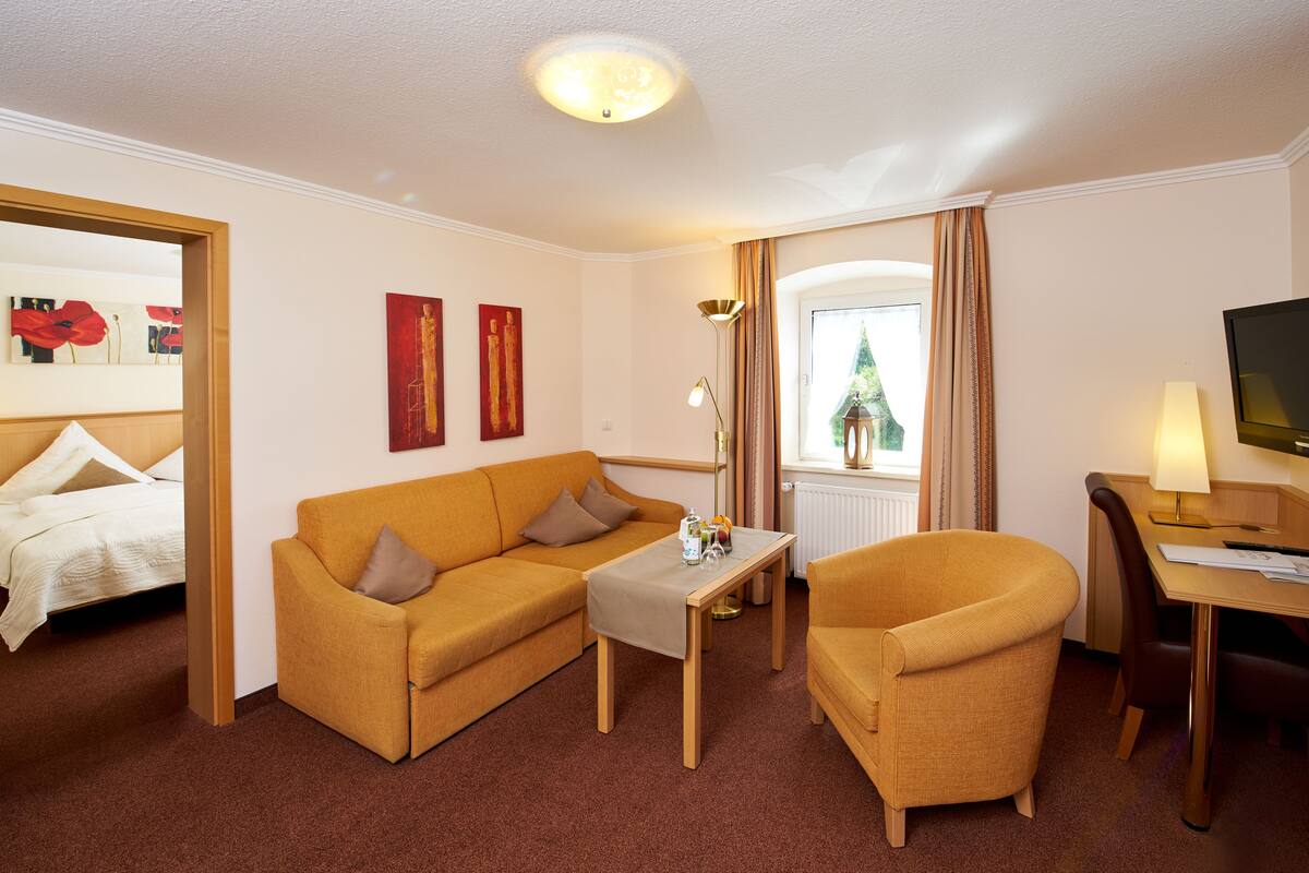 A hotel room with a sofa, armchair, small table, and a TV.