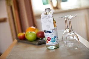 Una botella de agua mineral DAUNER con etiqueta, una bandeja de frutas y dos copas de vino vacías sobre una mesa.