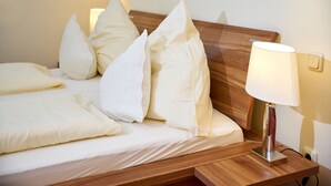 Una cama bien hecha con ropa blanca y almohadas, un cabecero de madera y una mesita de noche con una lámpara.
