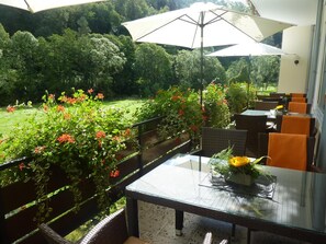 Une terrasse extérieure aménagée avec des meubles en osier, une table en verre et un parasol.