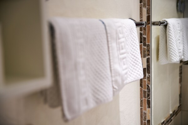 Un baño con pared de azulejos y toallero con toallas blancas.