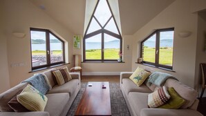 Ein Zimmer mit zwei Sofas, die zu einem großen Fenster mit Blick auf ein grasbewachsenes Feld und Berge ausgerichtet sind.