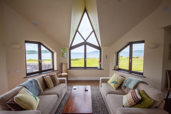 Una habitación con dos sofás orientados hacia una ventana grande con vistas a un campo de césped y montañas.