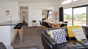 Una sala moderna con un sofá de cuero, comedor y cocina con un lavamanos y taburetes.