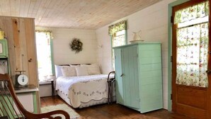 A cozy room with a wooden floor, a bed with a floral bedspread, a green wardrobe, and a wooden chair. - Taylor Made Bed and Breakfast (Spillville)