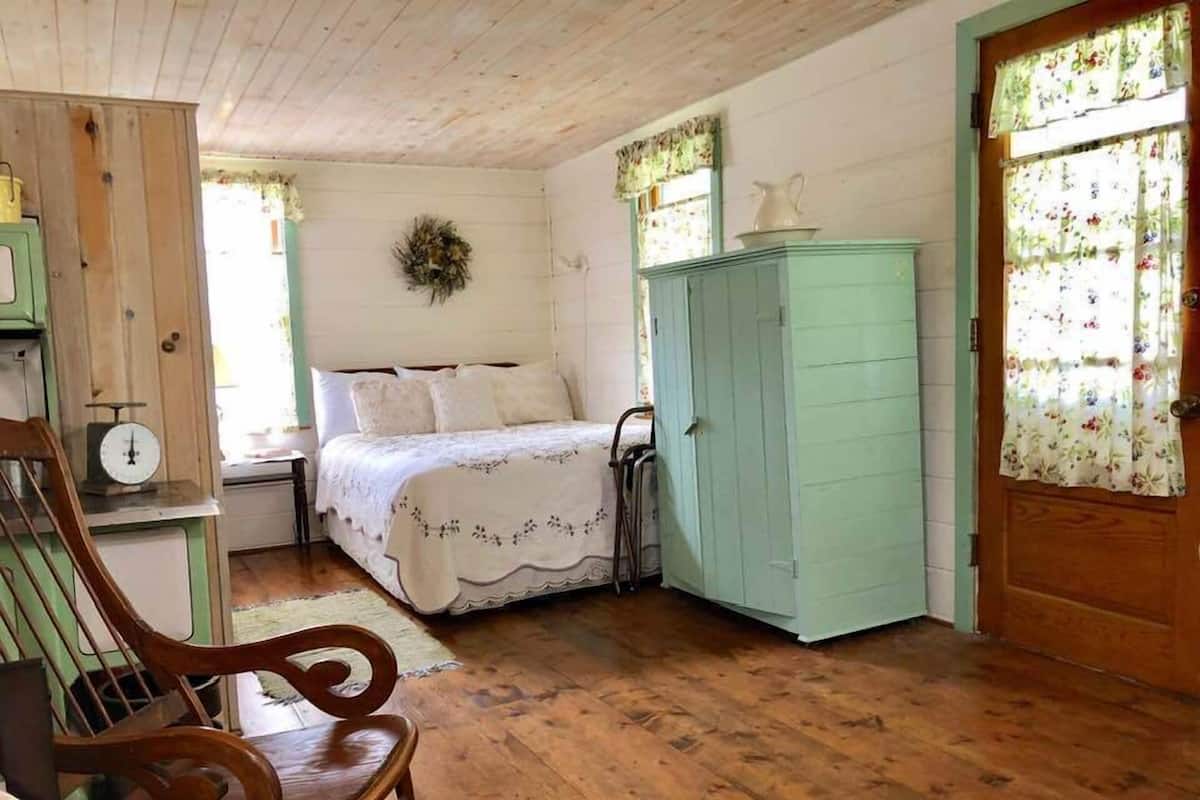 Una habitación acogedora con suelo de madera, una cama con colcha estampada, un armario verde y una silla de madera.