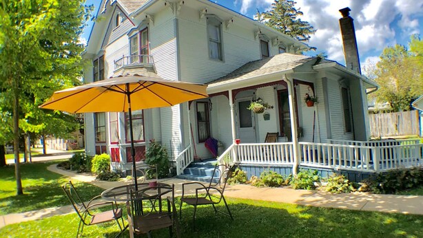 A two-story house with a porch, a chimney, and a table with chairs. - Taylor Made Bed and Breakfast (Spillville)