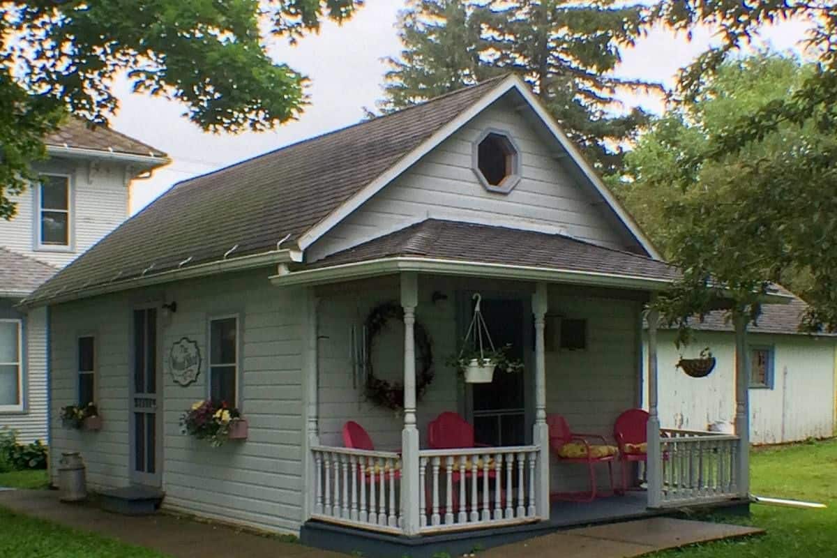 Una pequeña casa de una sola planta con un porche, una puerta principal y un ventanal.
