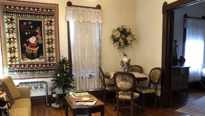 A cozy living room with a large Christmas-themed quilt, a small Christmas tree, and a dining area with a table and chairs. - Taylor Made Bed and Breakfast (Spillville)