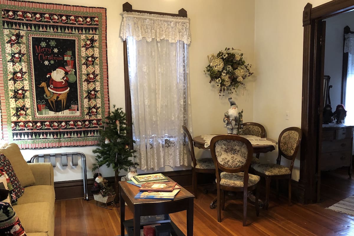Una sala acogedora con un colcha navideña grande, un árbol de Navidad pequeño y un comedor con mesa y sillas.