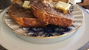 A plate with two pieces of toasted bread and a pat of butter on a decorative plate. - Taylor Made Bed and Breakfast (Spillville)