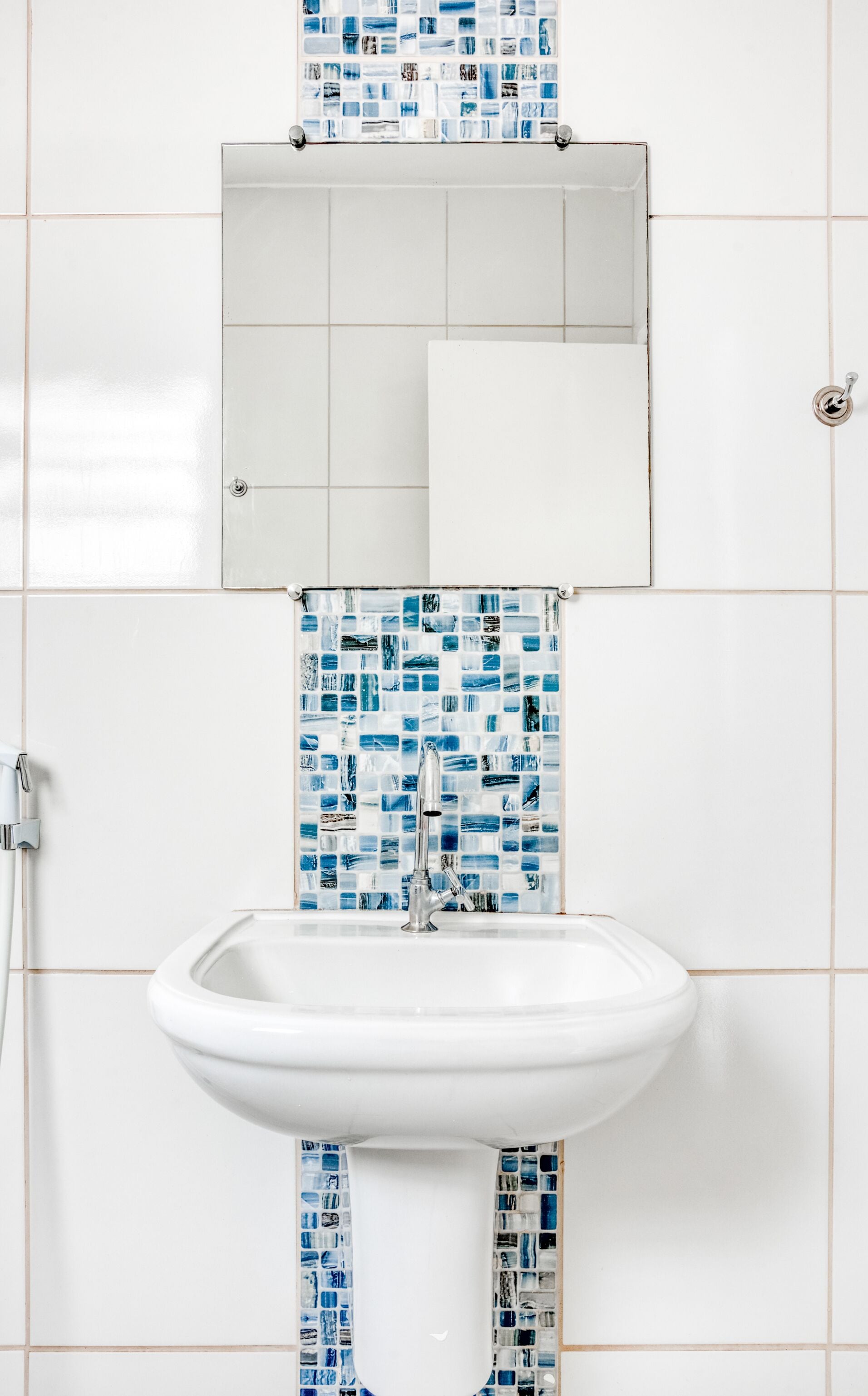 Un baño con un lavamanos blanco, un espejo encima y un salpicadero de azulejos con mosaicos azules.