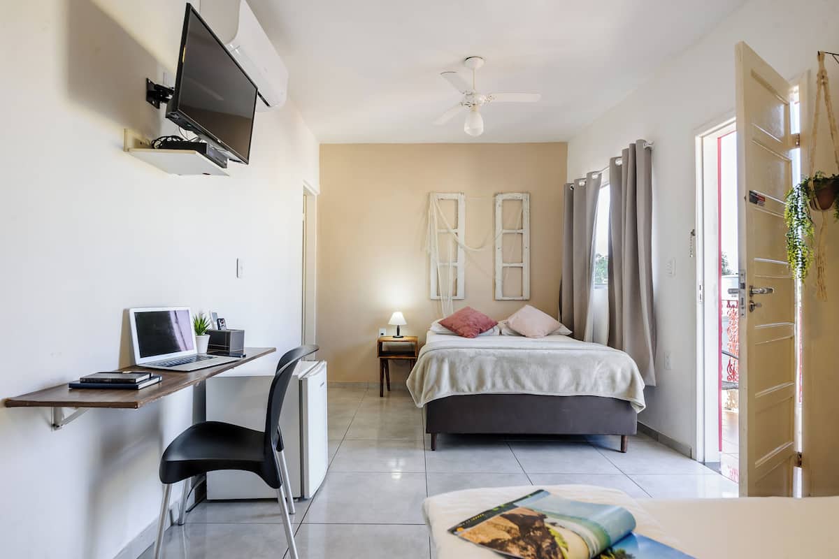 A bedroom with a bed, desk, chair, TV, and a ceiling fan.