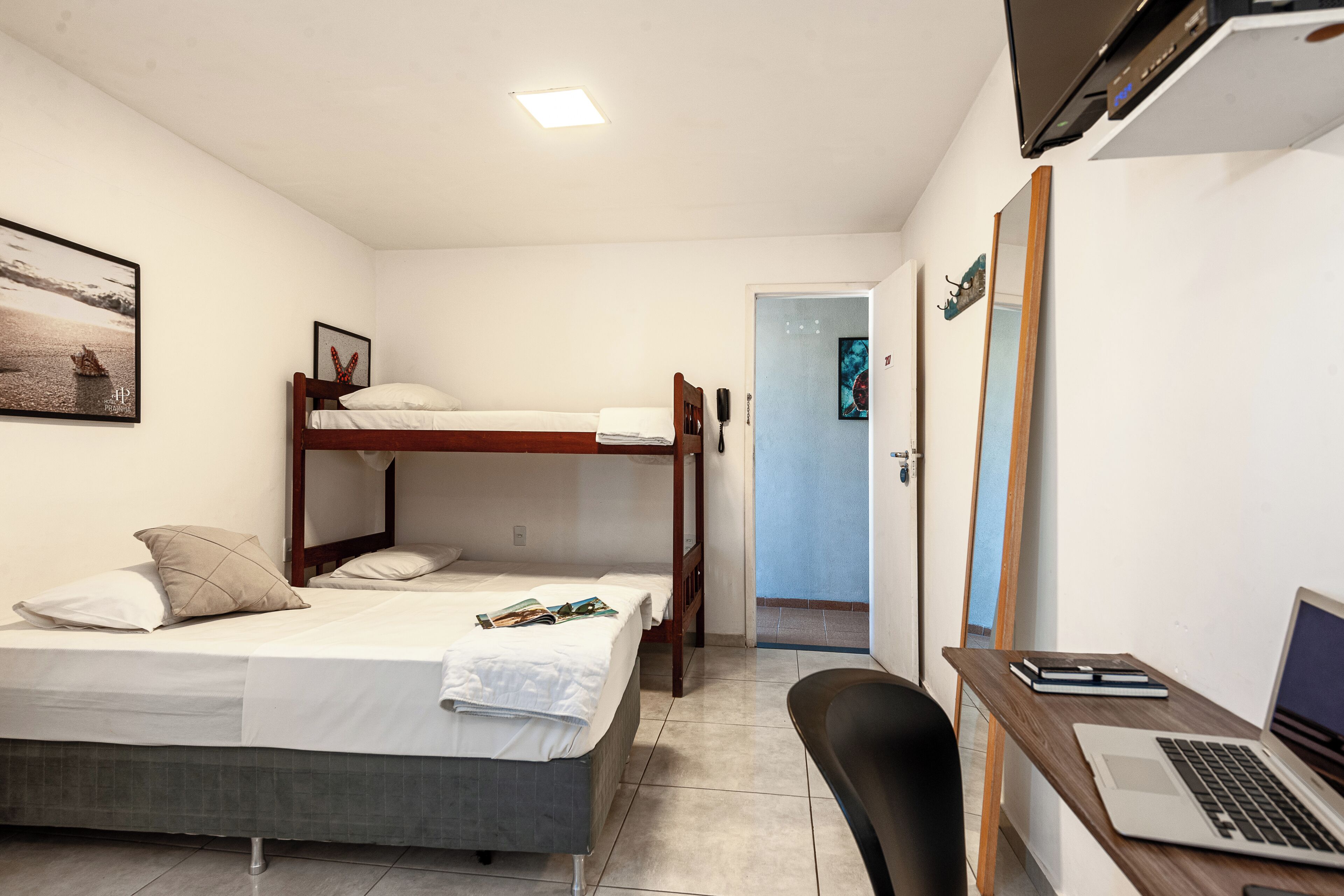A room with a bunk bed, a desk with a laptop, and a door leading to another room.