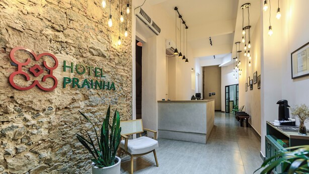 Un hall d’hôtel avec un mur en pierre, un comptoir d’accueil, un espace salon et des luminaires suspendus.