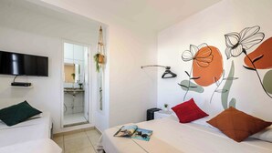 Une chambre d’hôtel avec un lit, un téléviseur fixé au mur et une salle de bain visible à travers une porte ouverte.