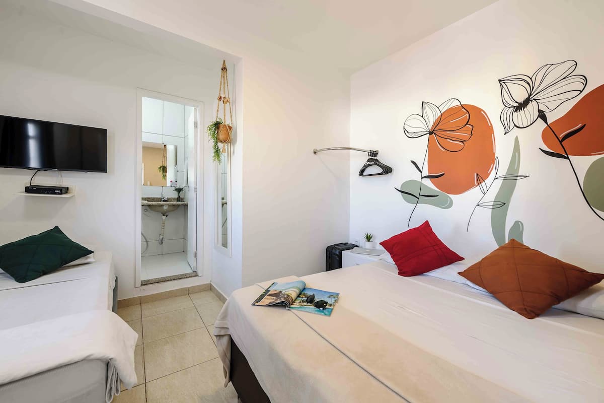A hotel room with a bed, a TV mounted on the wall, and a bathroom visible through an open door.